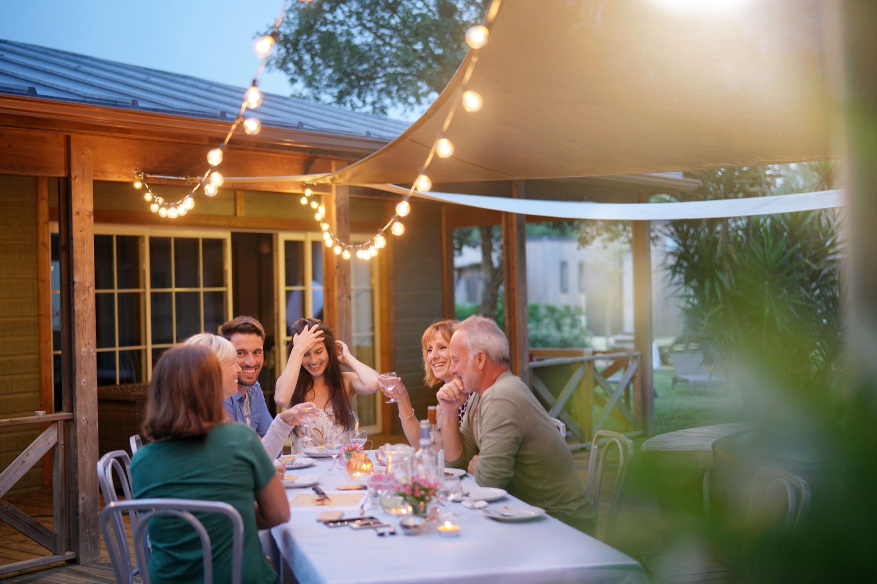 Friends eating together at an outdoor table under festoon lights